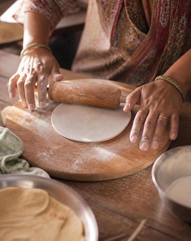 Hands rolling out fresh roti dough on a wooden board